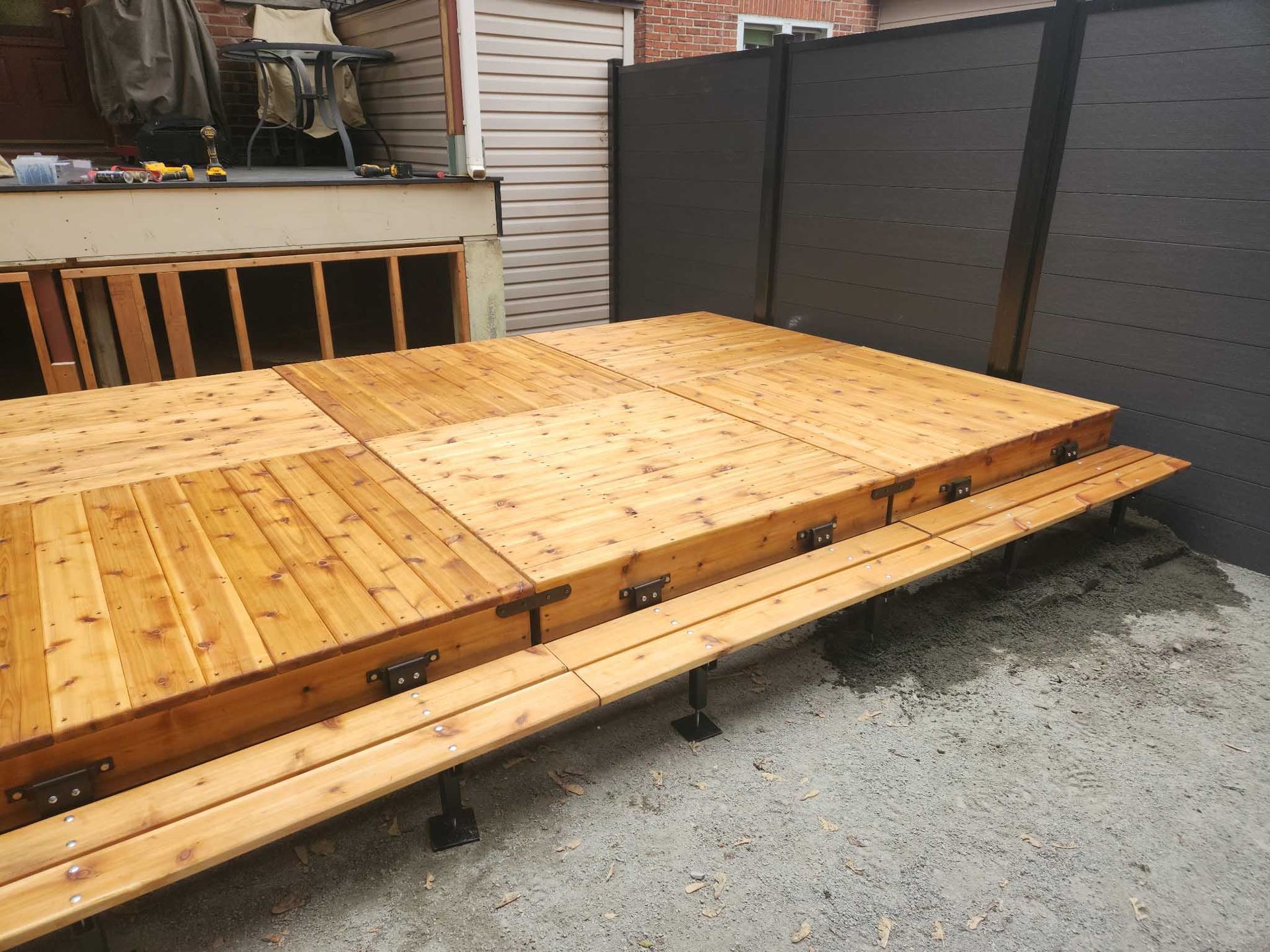 Terrasse en bois avec bancs intégrés, aménagée dans un espace extérieur recouvert de gravier, à côté d'une clôture noire.