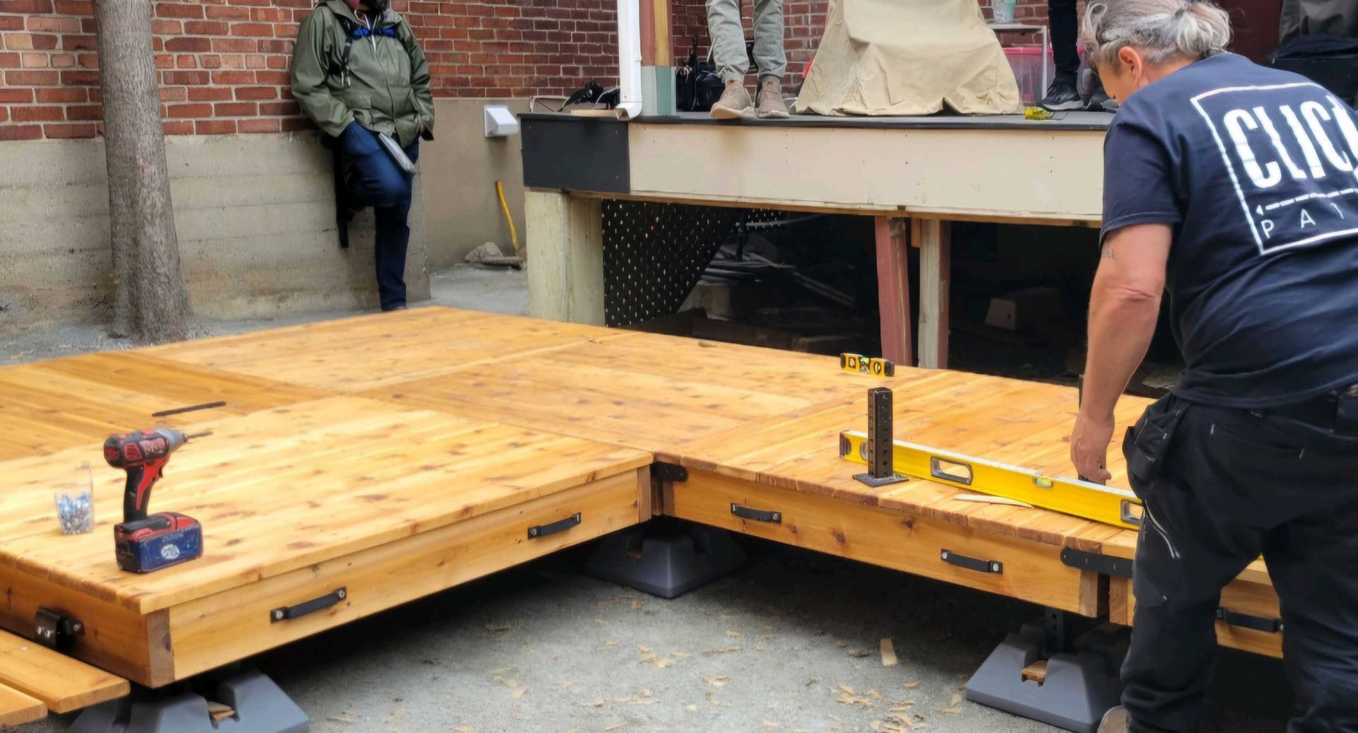 Personne construisant une terrasse en bois à l'extérieur, à l'aide d'un niveau et d'outils.