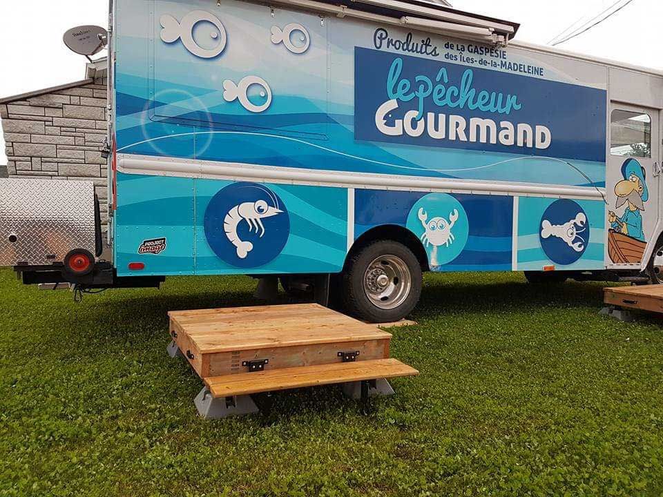 Camion-restaurant « Le Pêcheur Gourmand » décoré de motifs de fruits de mer. Plateforme en bois sur pelouse.