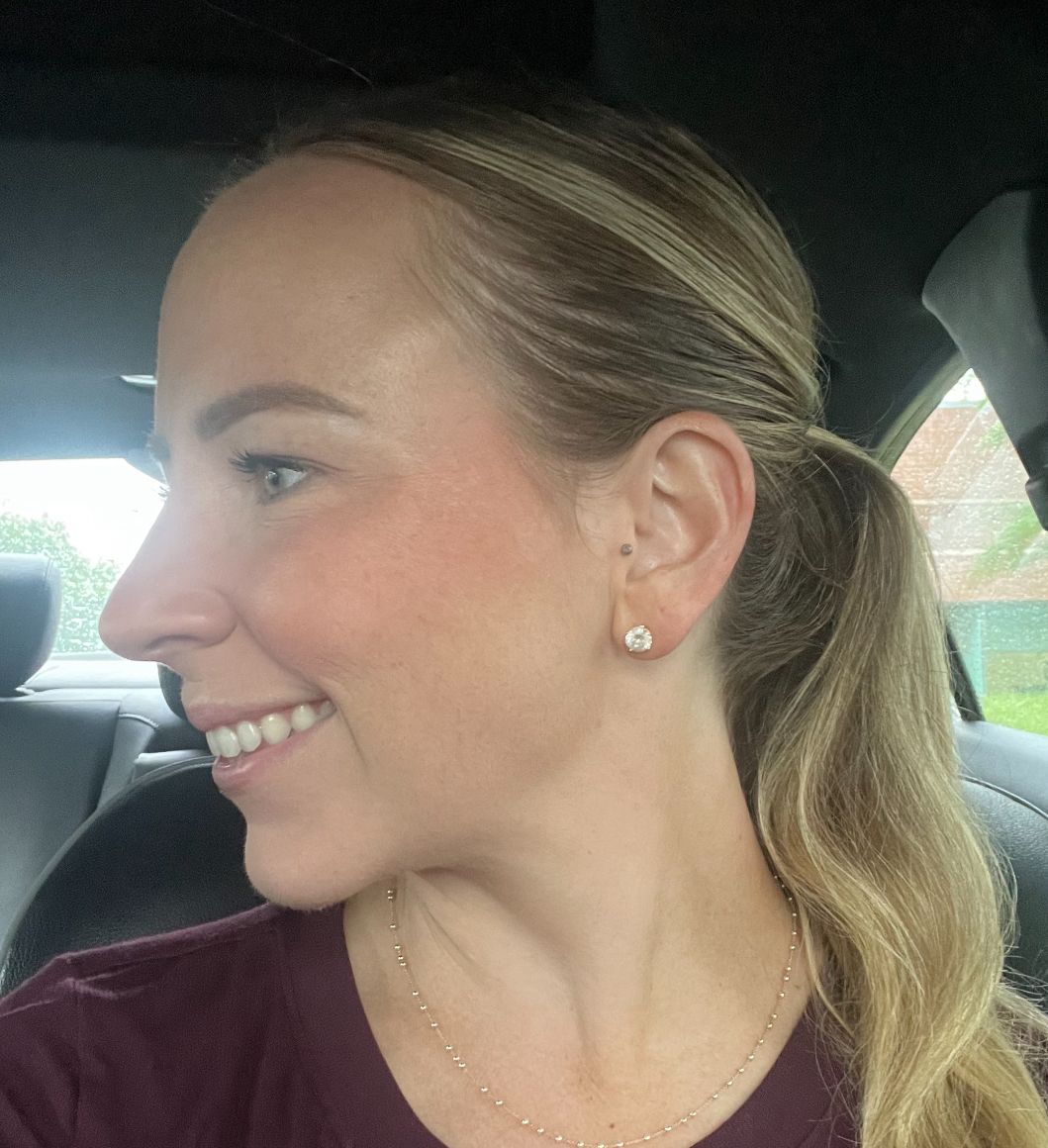 A woman wearing earrings and a necklace is smiling while sitting in a car.