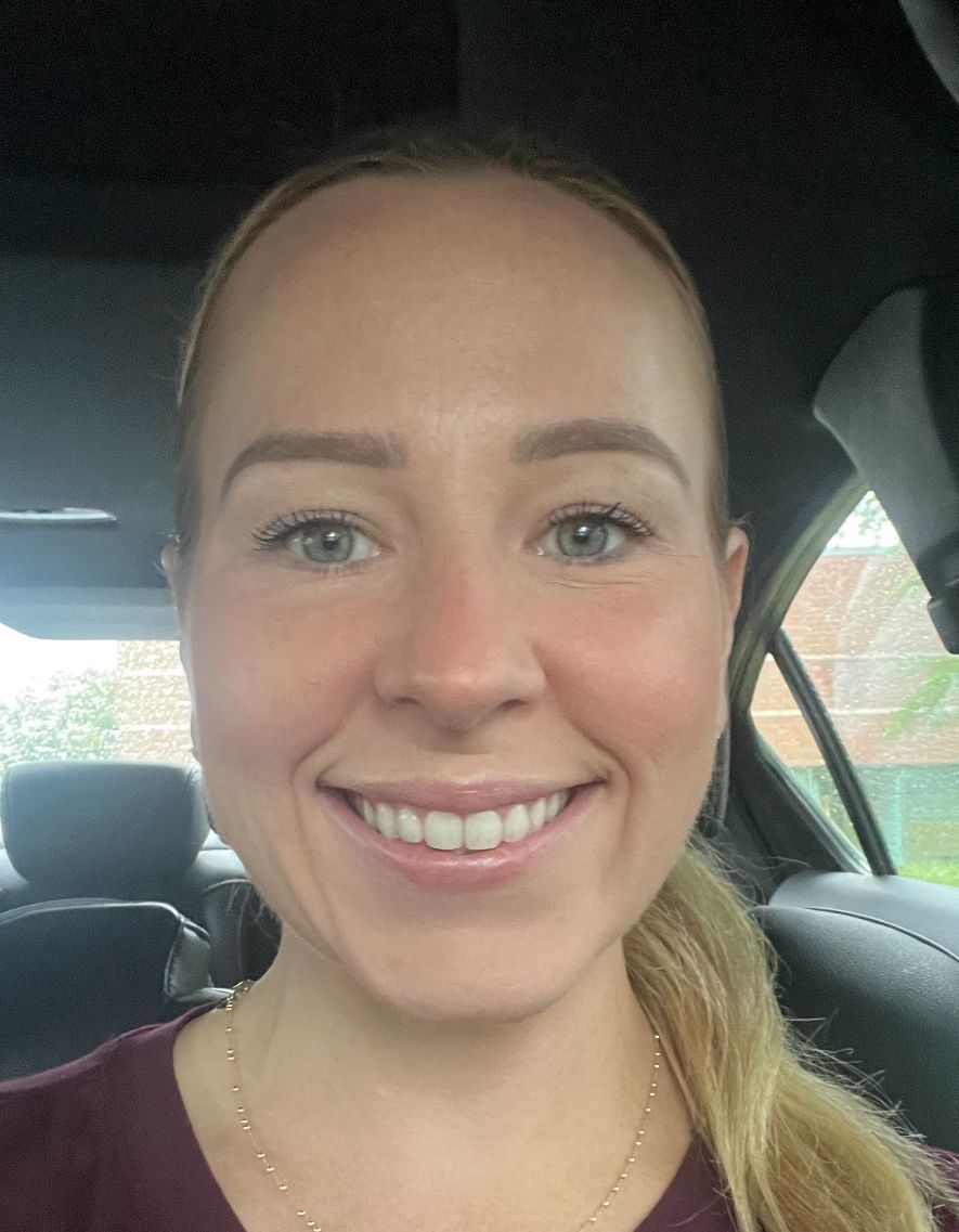 A woman is smiling while sitting in the back seat of a car.
