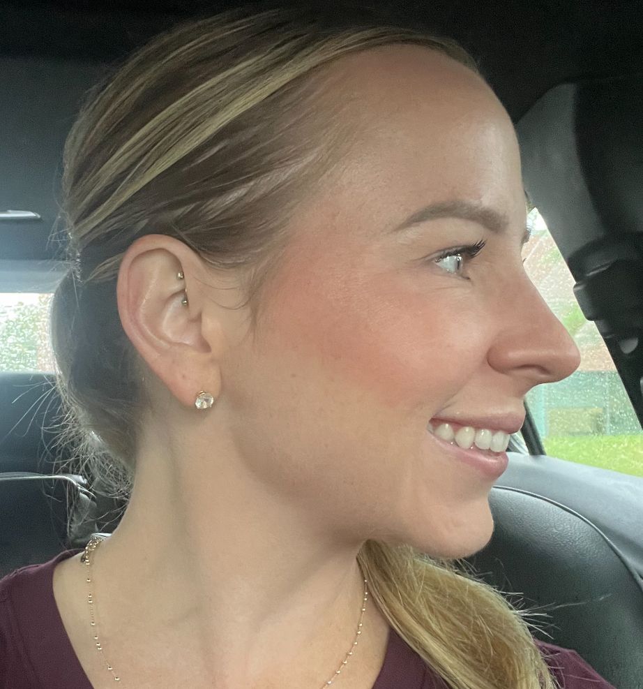 A woman wearing earrings is smiling while sitting in a car