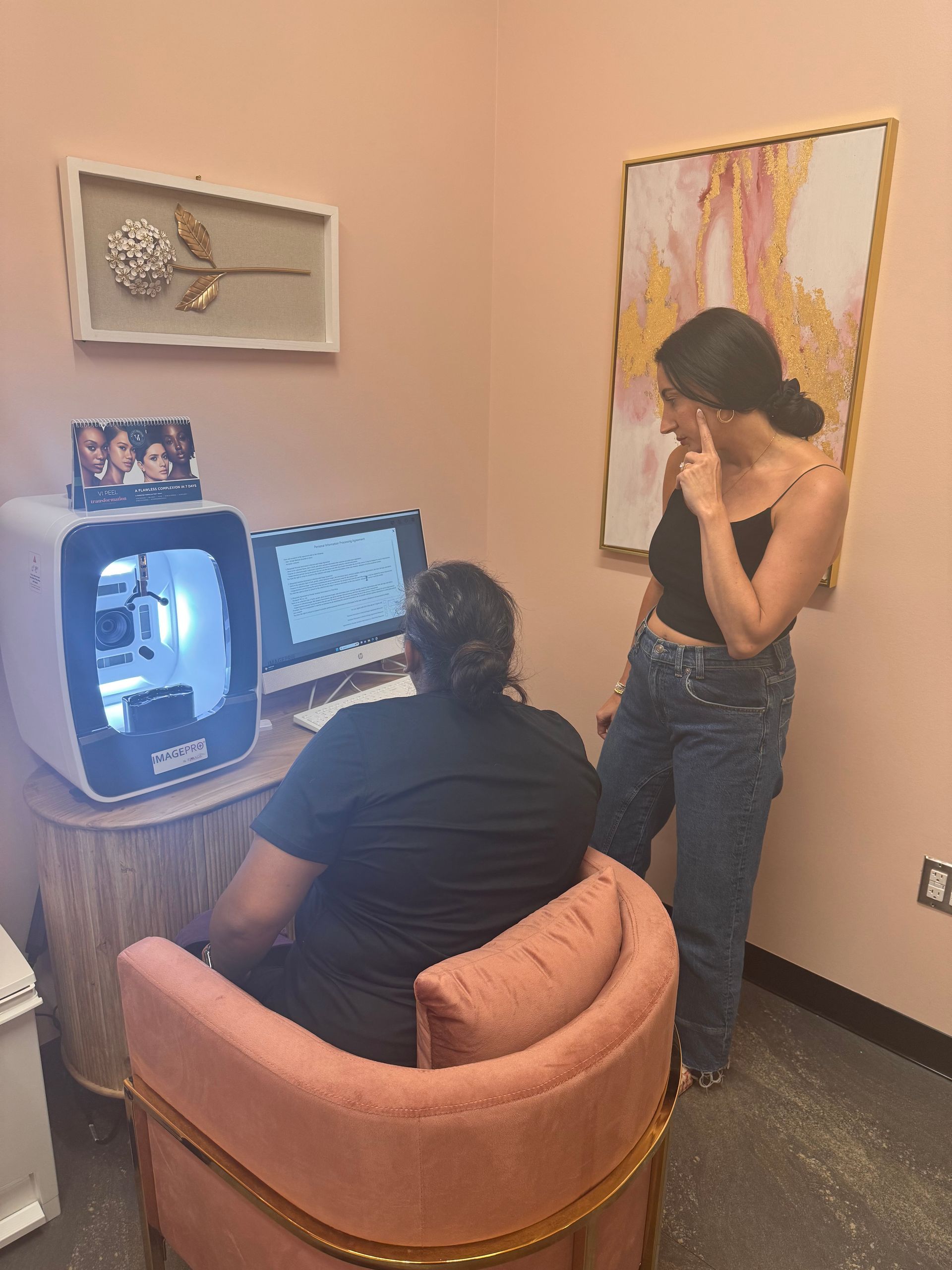 A woman is standing next to a woman sitting in a chair in front of a computer.