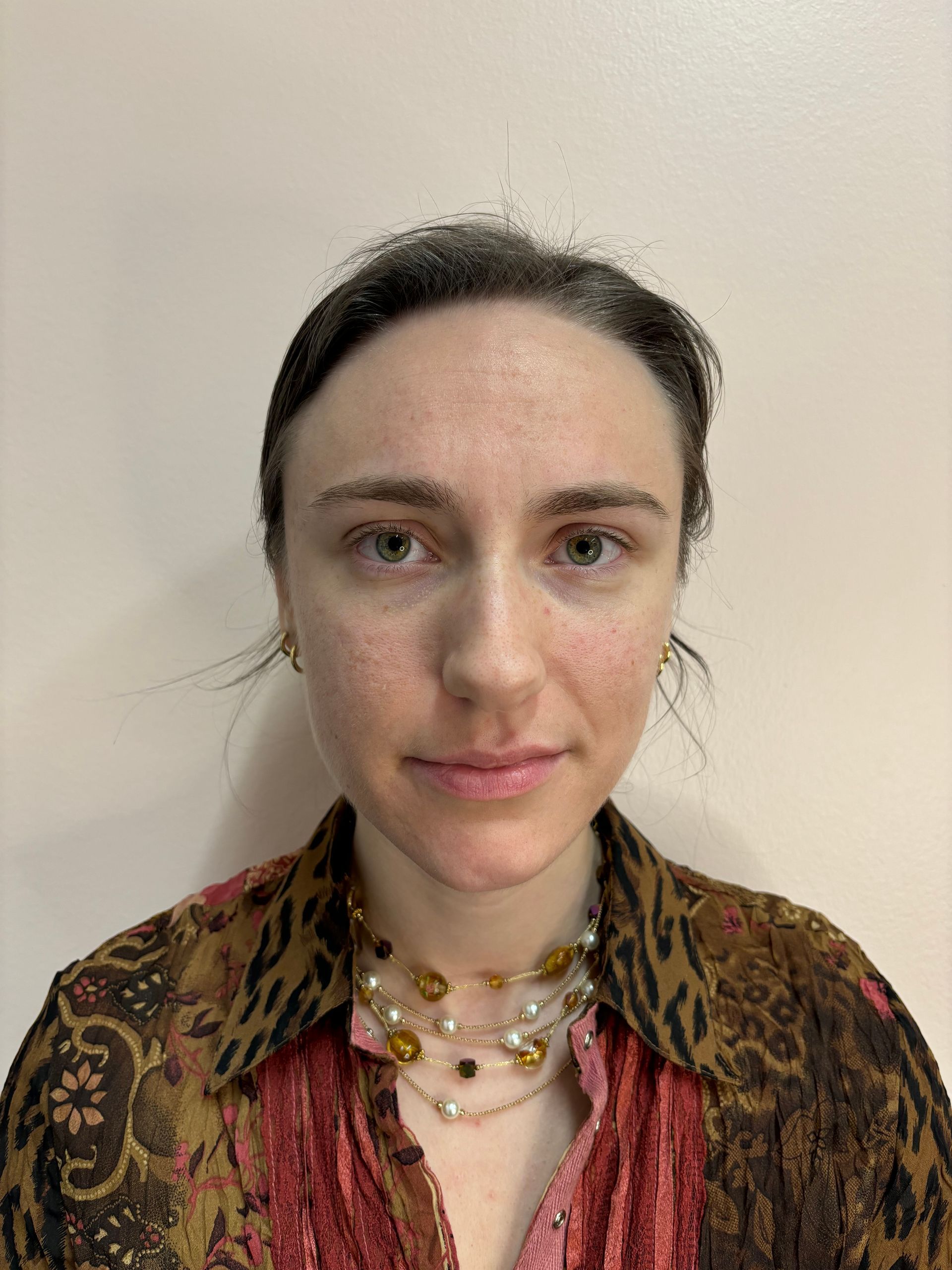 A woman wearing a leopard print shirt and a necklace is standing in front of a white wall.