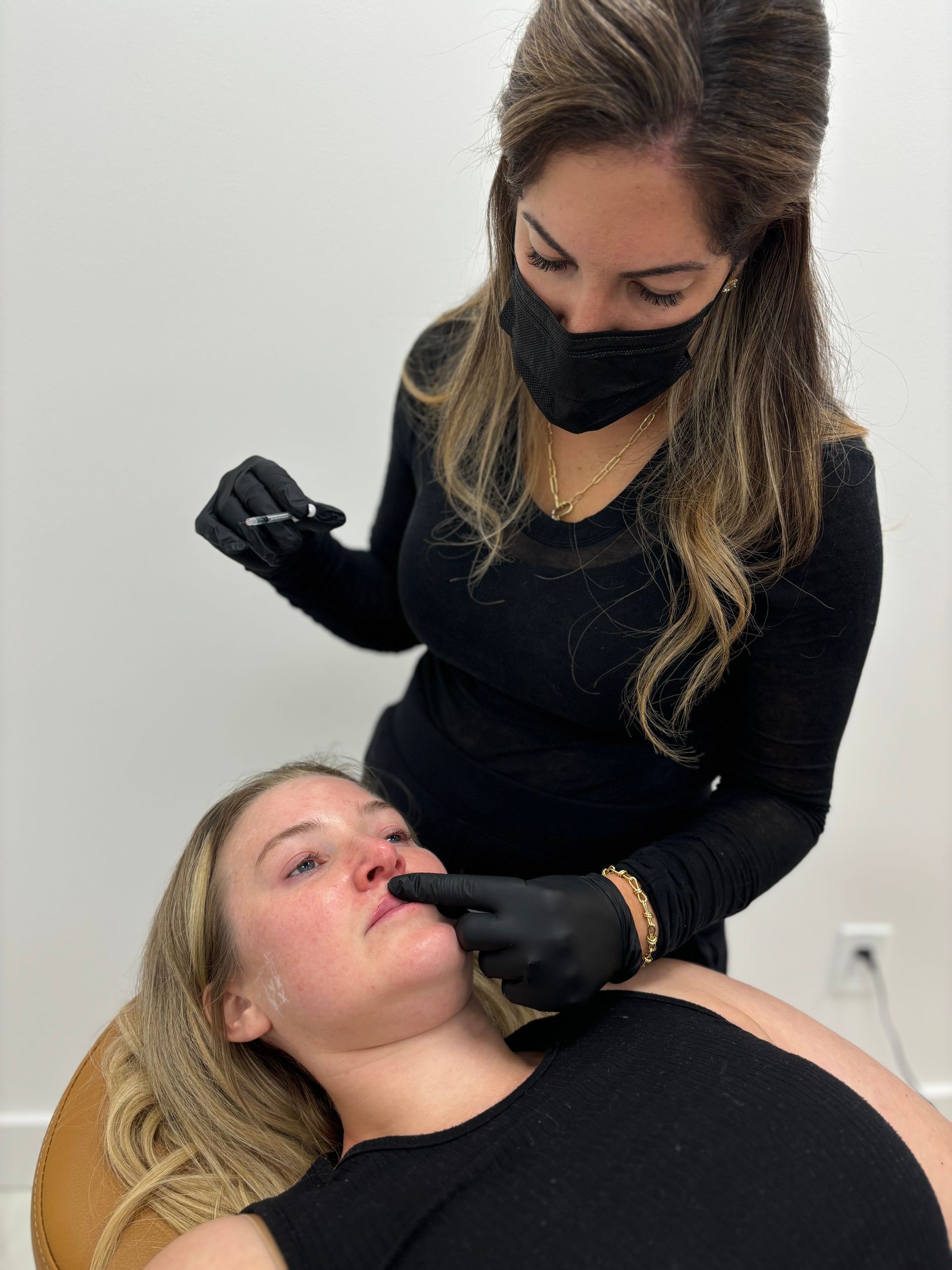 A woman wearing a mask is giving a woman an injection in her face