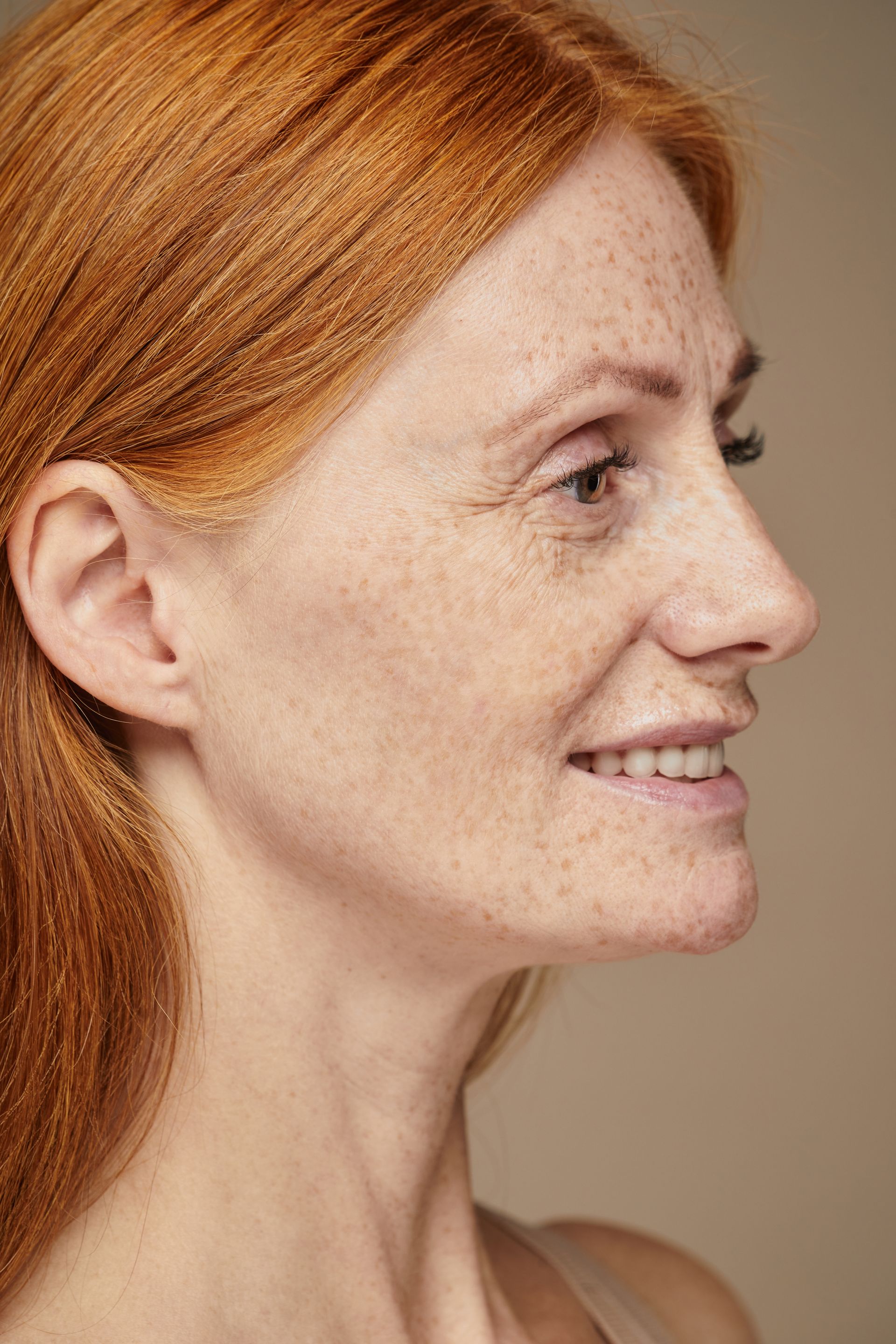 Woman with red hair and freckles, smiling in profile against a neutral background.