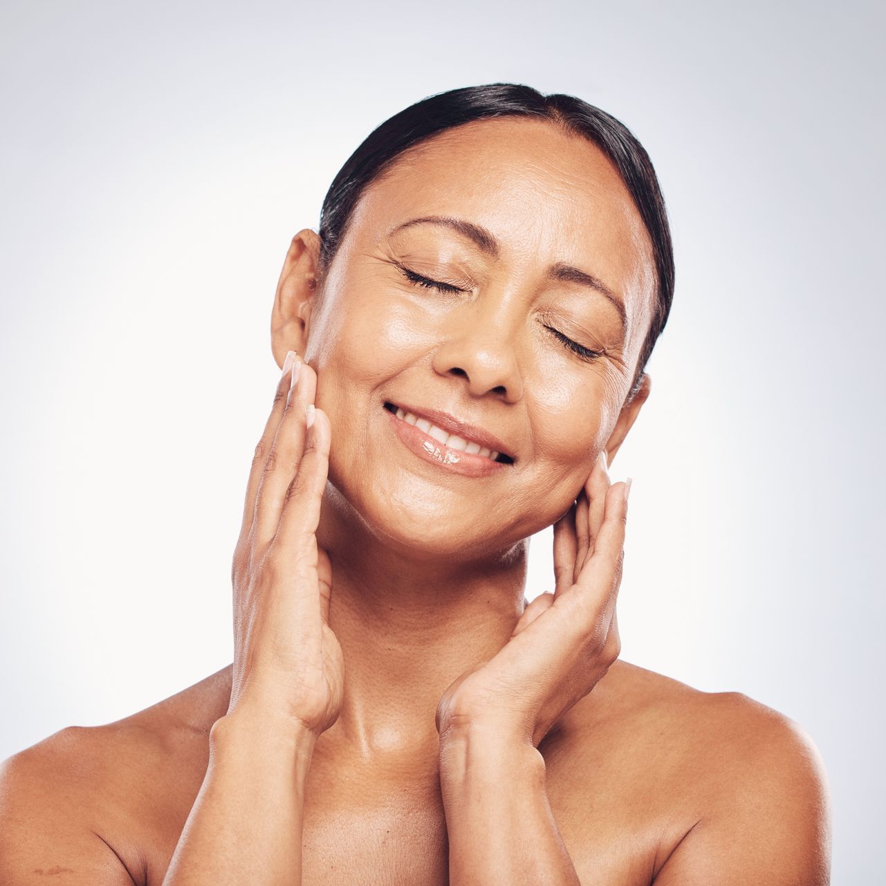 A woman is touching her face with her hands and smiling.