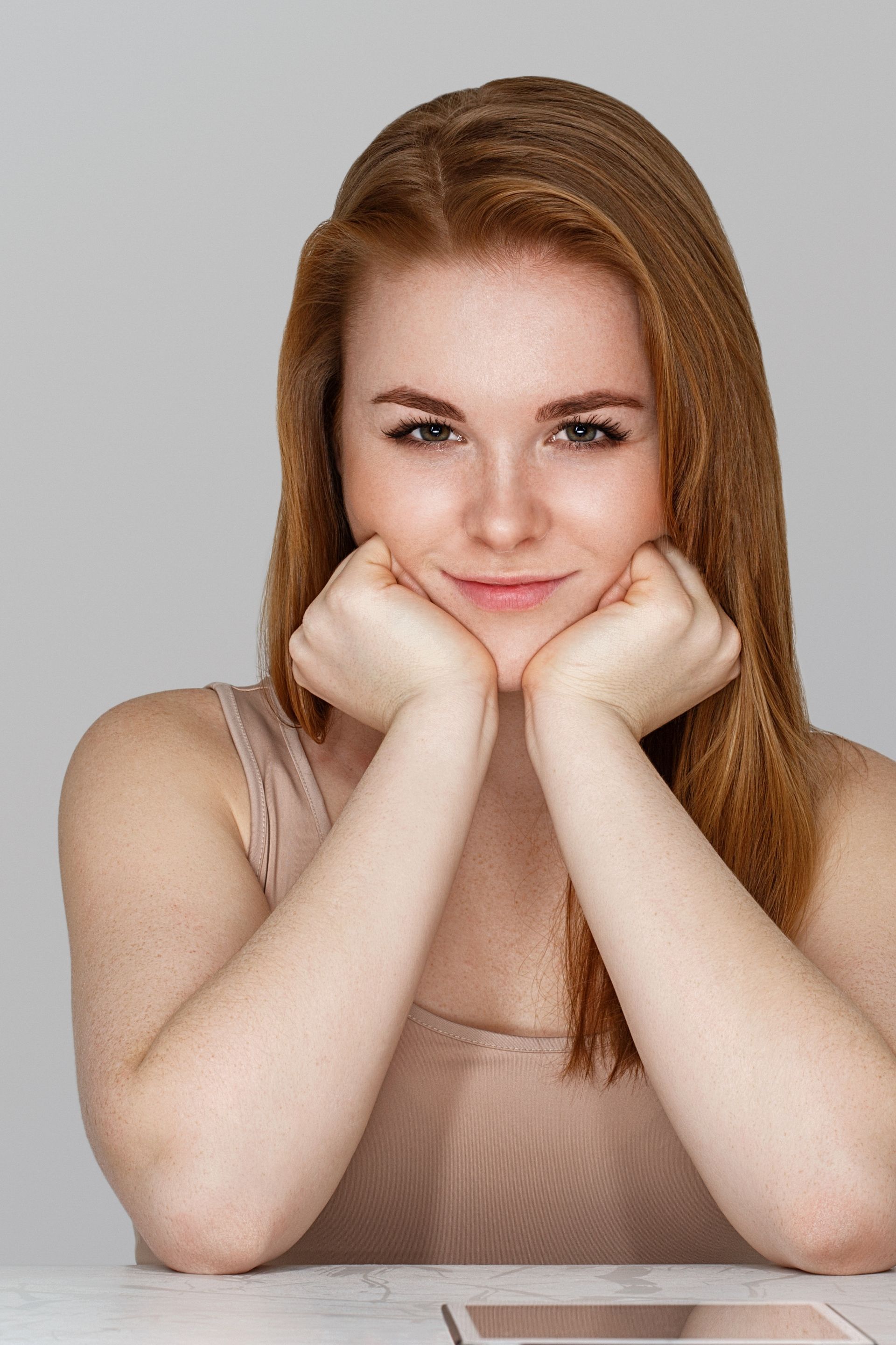 A woman with red hair is sitting at a table with her hands on her chin.