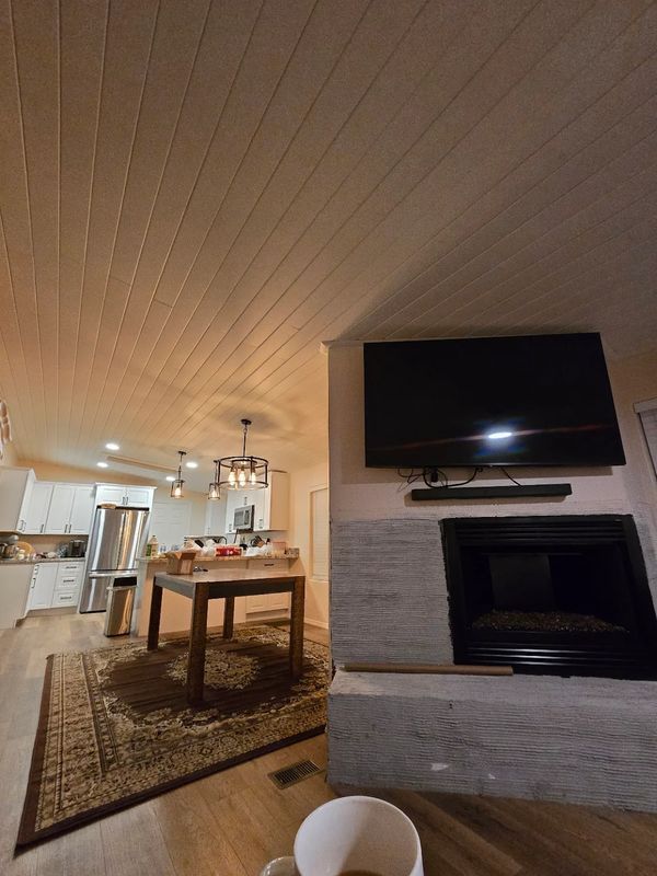 Open-plan living room with fireplace, wall-mounted TV, dining table, and kitchen in the background