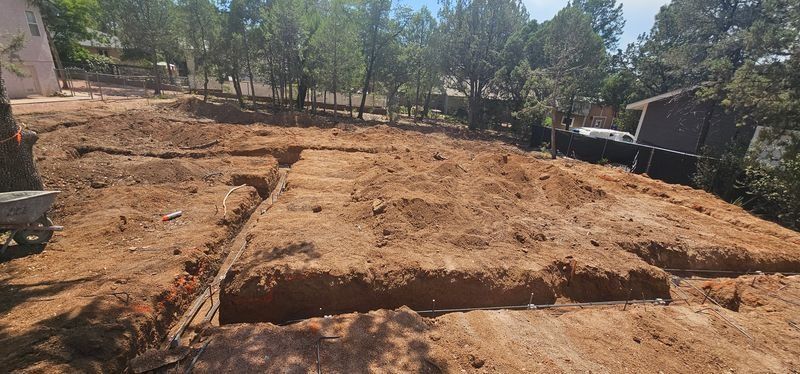 Dry, cleared dirt plot with trees in the background and a small building to the right.