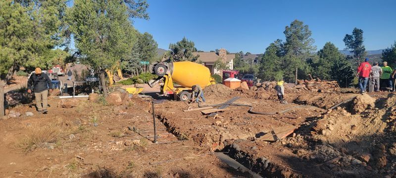 Mudslide cleanup scene with workers, a yellow cement mixer, and debris under a blue sky