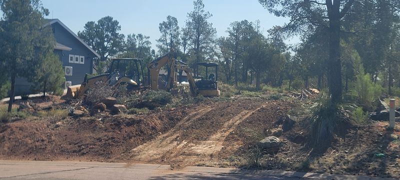 Bulldozer clearing dirt on a sloped lot beside a house and trees