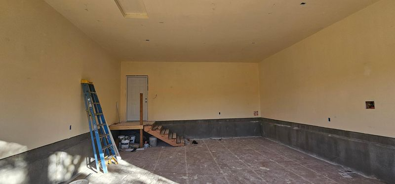 Partially renovated room with tan walls, dark wainscoting, blue ladder, and construction debris on the floor