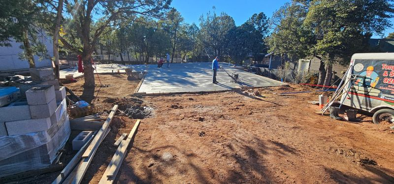 Construction site with a dirt path, trees, stacked materials, and workers in the distance