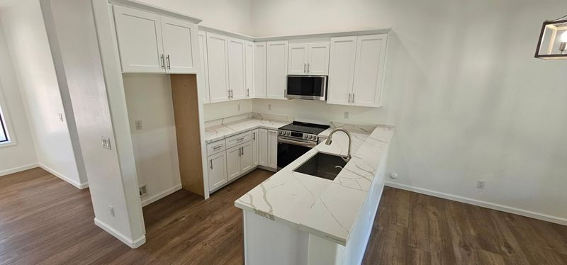 Bright white kitchen with island, black appliances, wood floors, and open doorway to a pantry