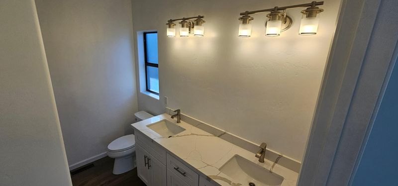 Modern bathroom with double vanity, wall lights, mirror, and a window.