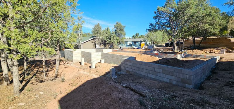 Outdoor construction site with concrete retaining walls, dirt ground, and trees under a clear blue sky