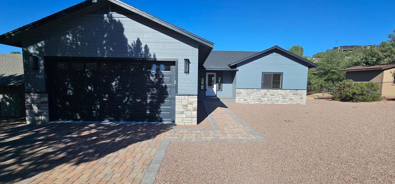 Modern house with dark garage door, paved driveway, and gravel yard under a clear blue sky