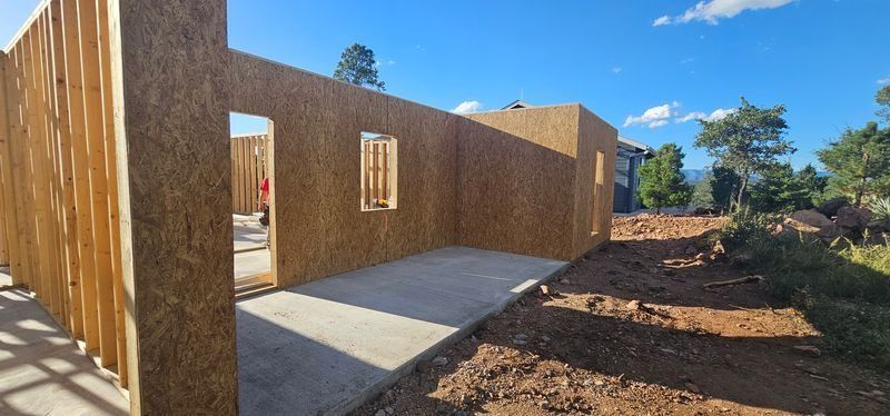 Partially built wooden house exterior with concrete slab and open framing in a rural setting