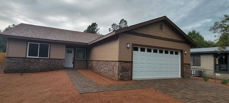 Single-story brick house with a two-car garage and gravel driveway under a cloudy sky