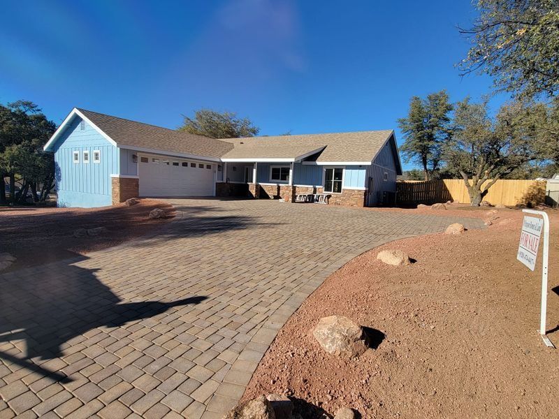 Single-story suburban house with blue garage, brick driveway, and desert landscaping under a clear sky