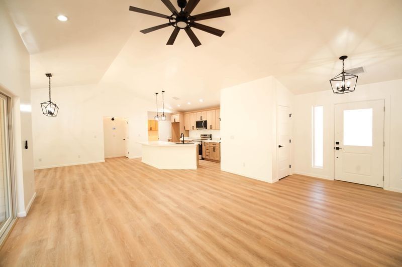 Bright open living room with wood floors, white walls, ceiling fans, and a kitchen area.