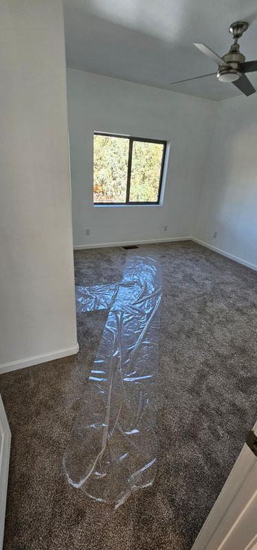 Empty white room with gray tile floor, ceiling fan, and window letting in daylight