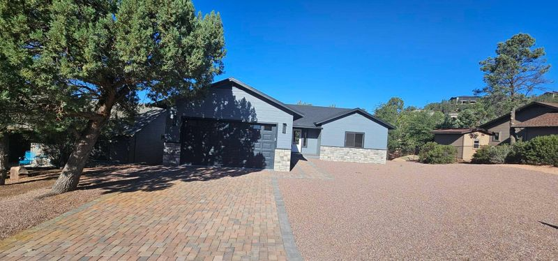Suburban house with blue-gray exterior, brick driveway, and trees under a clear sky