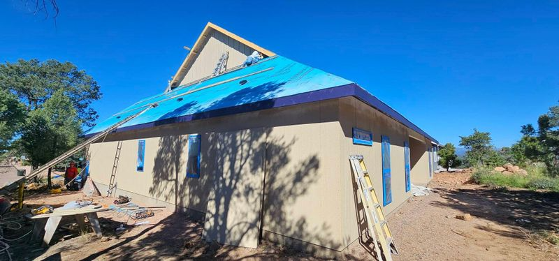 Partially built house with beige walls and a blue tarp roof under a clear sky