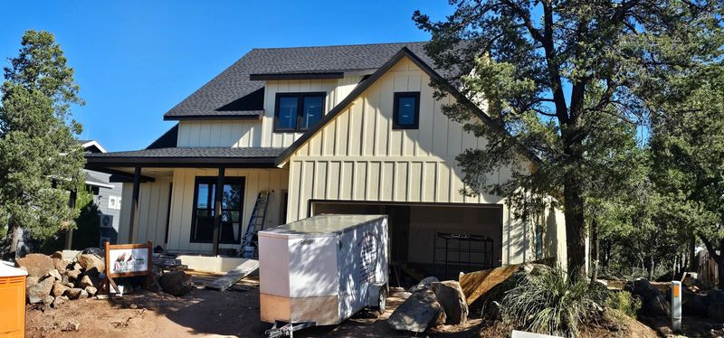 New house exterior with white siding, dark roof, and construction materials in front yard