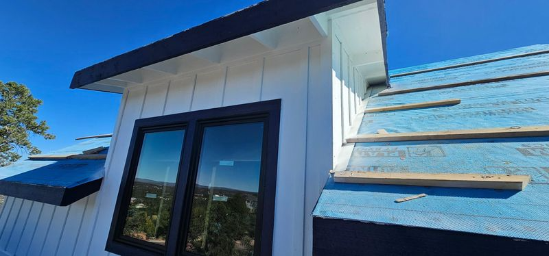 Roofline with white trim, black-framed windows, and blue roof against a clear sky