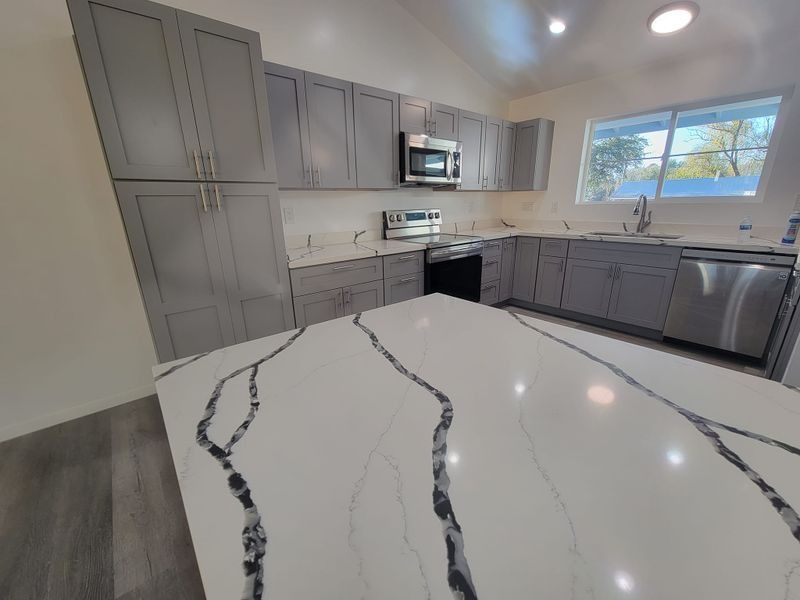 Modern gray kitchen with marble island, stainless appliances, and a window over the sink