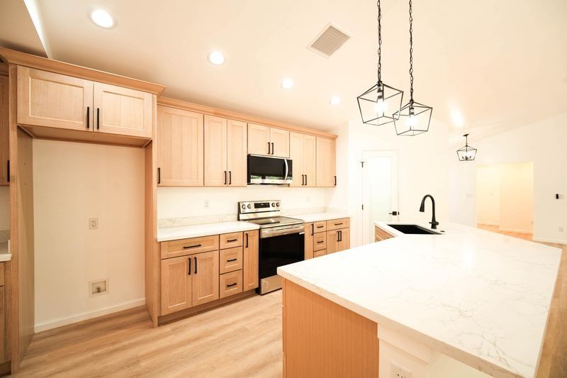 Bright modern kitchen with light wood cabinets, white island, and pendant lights