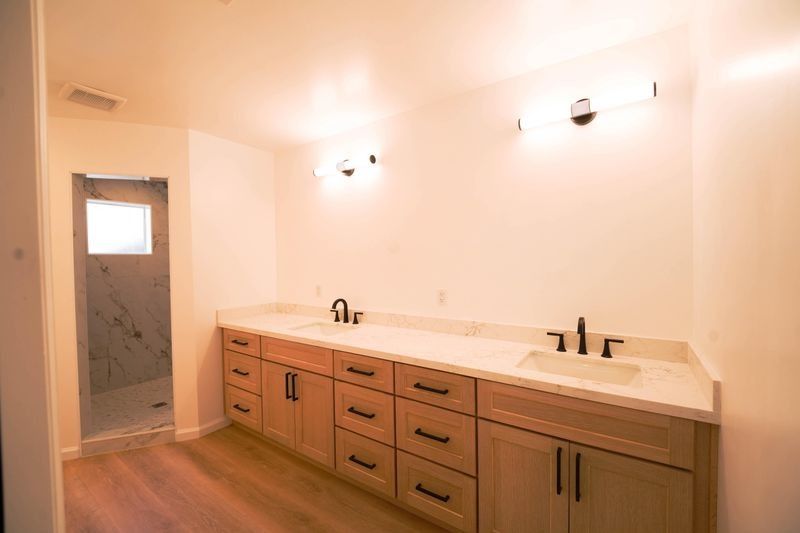 Modern bathroom with long double vanity, wood cabinets, white countertops, and wall sconces.