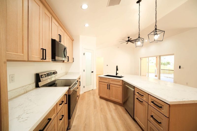 Bright modern kitchen with light wood cabinets, white countertops, stainless appliances, and pendant lights