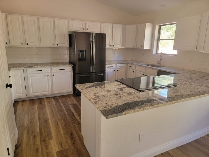 Bright modern kitchen with white cabinets, granite island, black refrigerator, and wood-look flooring