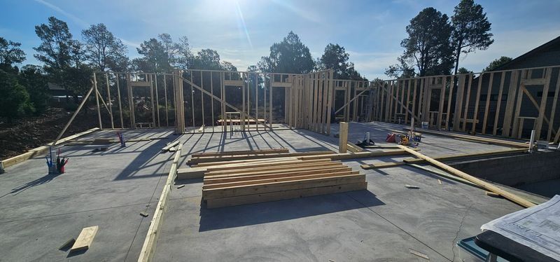 Wood-framed houses under construction on a concrete foundation in bright sunlight