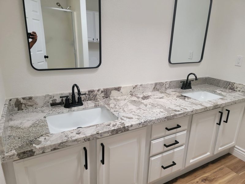 Modern bathroom vanity with double sinks, black faucets, gray marble countertop, and wall mirrors.