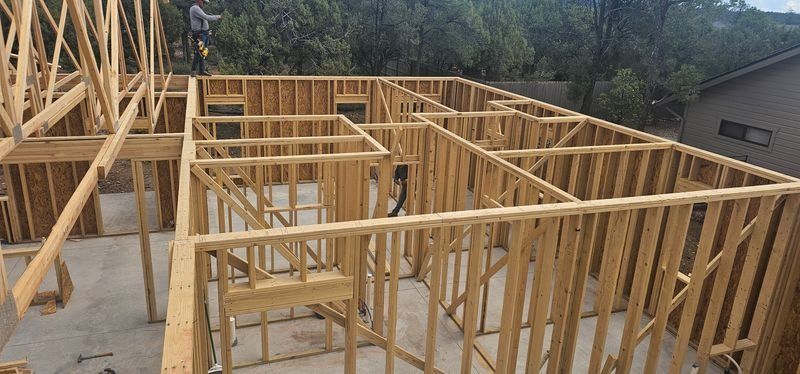 Wooden house framing under construction on a concrete slab, with exposed wall studs and roof trusses.