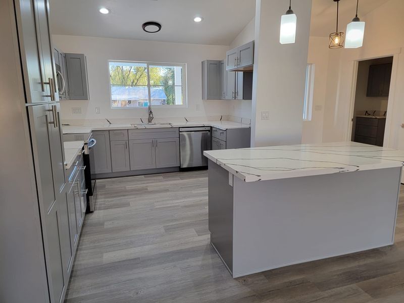Modern kitchen with gray cabinets, white island, stainless appliances, and pendant lights