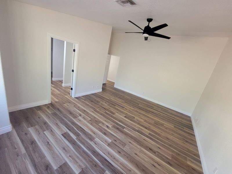 Empty modern bedroom with wood-look flooring, white walls, ceiling fan, and open doorway