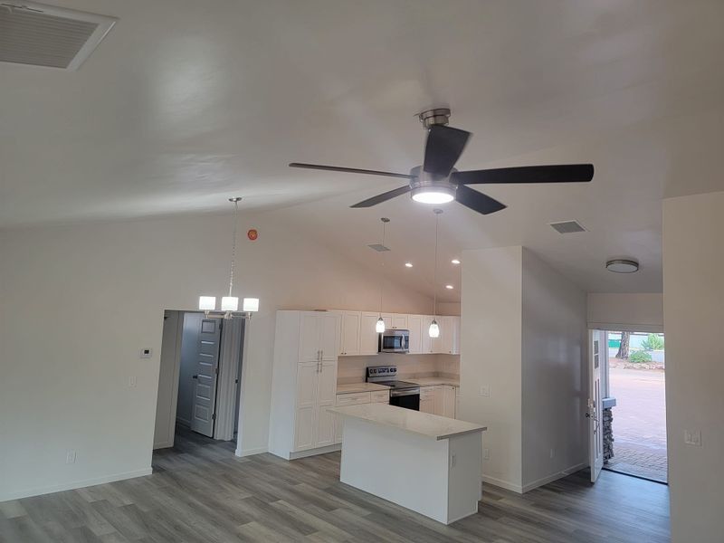 Empty modern kitchen and living area with white walls, island, ceiling fan, and open front door