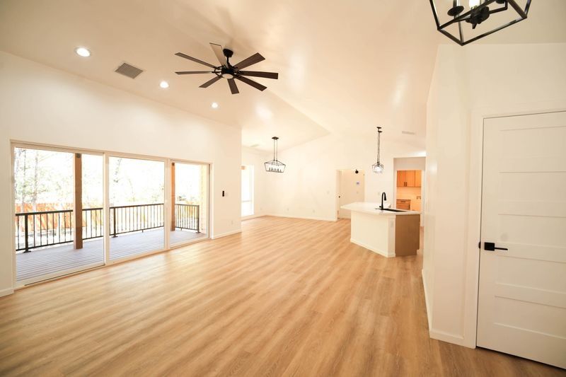 Spacious empty living room with light wood floors, white walls, ceiling fans, and large sliding glass doors.