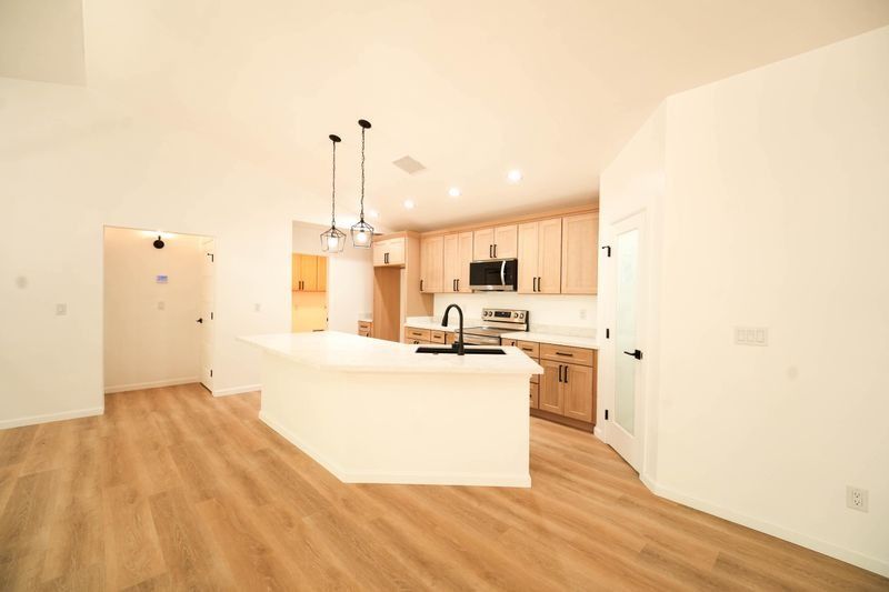 Bright open kitchen with wood floors, white cabinets, and a curved breakfast bar in an empty room