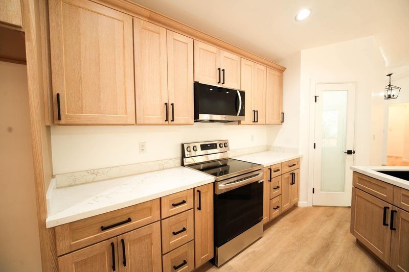Bright modern kitchen with light wood cabinets, white countertops, stainless stove, microwave, and wood floor