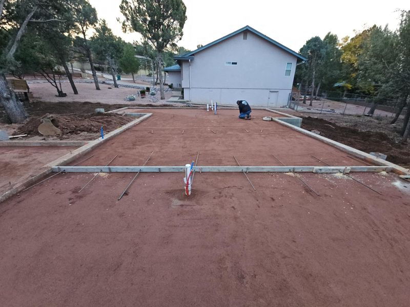 Roughly graded red dirt lot with forms and a white building in the background at dusk
