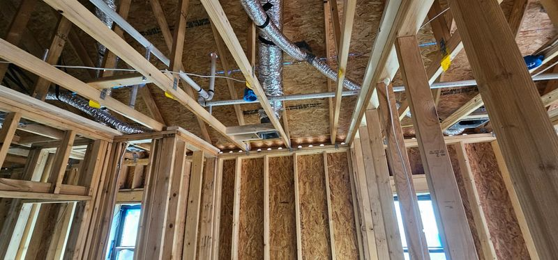 Interior of a wooden house under construction with exposed wall studs, ceiling joists, and roof trusses
