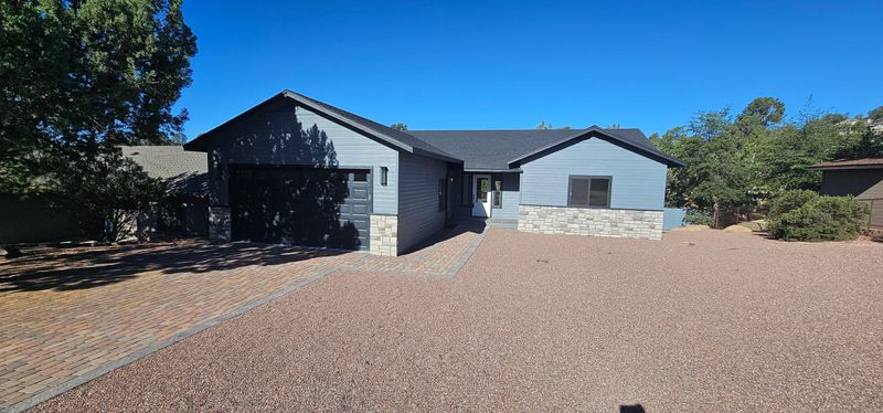 Single-story gray house with a garage and gravel front yard under a clear blue sky