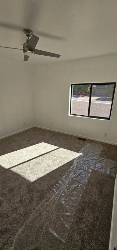 Empty unfurnished room with ceiling fan, tiled floor, and sunlight through a window