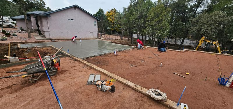 Graded dirt lot with survey stakes, tools, and a house in the background at a construction site